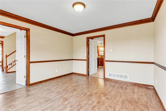 spare room with light wood-type flooring, visible vents, crown molding, baseboards, and stairs