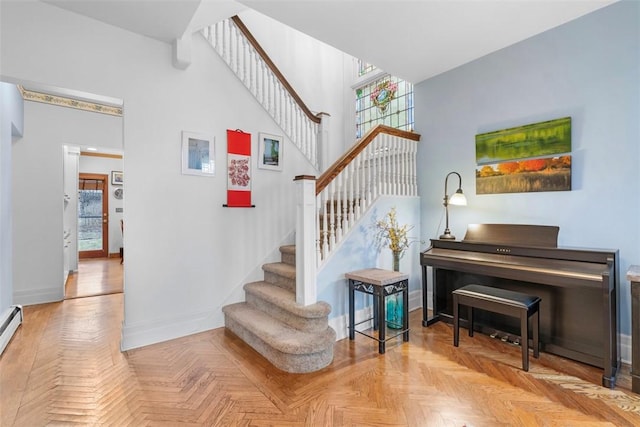 stairs with a baseboard heating unit, baseboards, and a high ceiling