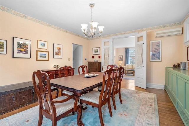 dining area with a notable chandelier, baseboards, a wall unit AC, and wood finished floors