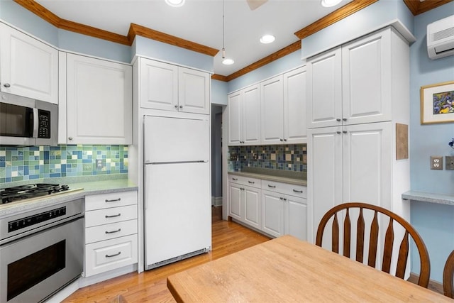 kitchen with appliances with stainless steel finishes, white cabinetry, light countertops, and a wall unit AC