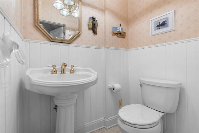 bathroom featuring wallpapered walls, toilet, and wainscoting