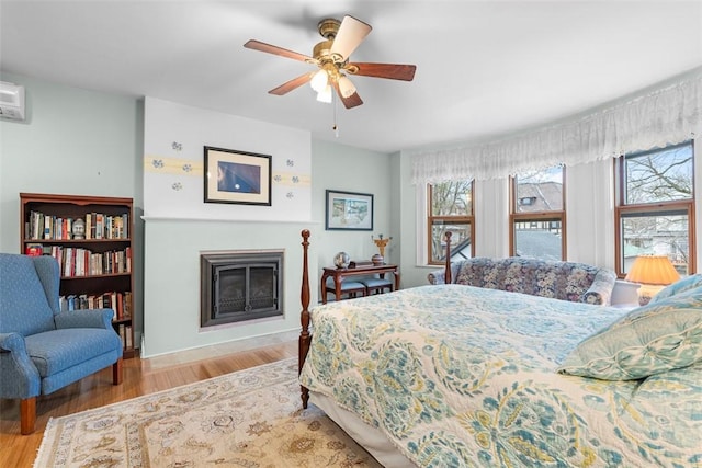 bedroom featuring a glass covered fireplace and wood finished floors