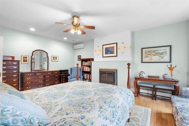 bedroom with wood finished floors, a wall mounted AC, recessed lighting, a glass covered fireplace, and baseboard heating