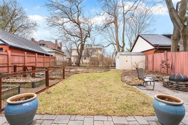 view of yard with a shed, a vegetable garden, a fenced backyard, an outdoor structure, and a fire pit