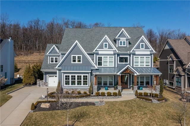 view of front facade featuring a front lawn, driveway, a standing seam roof, stone siding, and covered porch