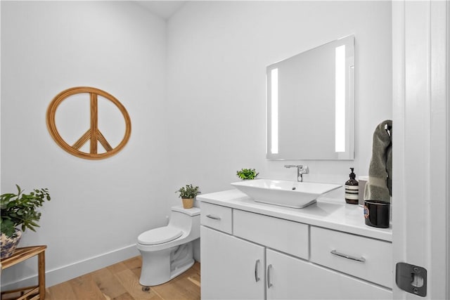 bathroom featuring baseboards, toilet, wood finished floors, and vanity