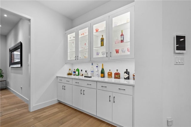 bar featuring light wood-style flooring, baseboards, and a dry bar