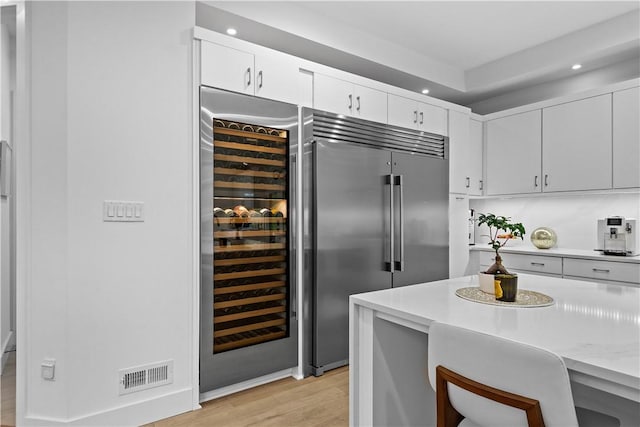 kitchen with visible vents, stainless steel built in fridge, light countertops, wine cooler, and light wood-style floors