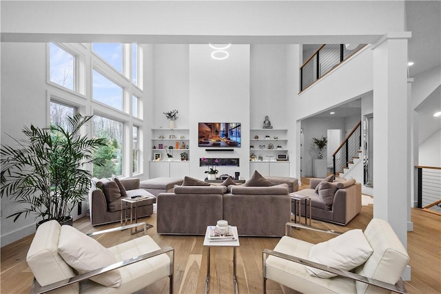 living area featuring stairway, light wood-style flooring, built in features, and baseboards