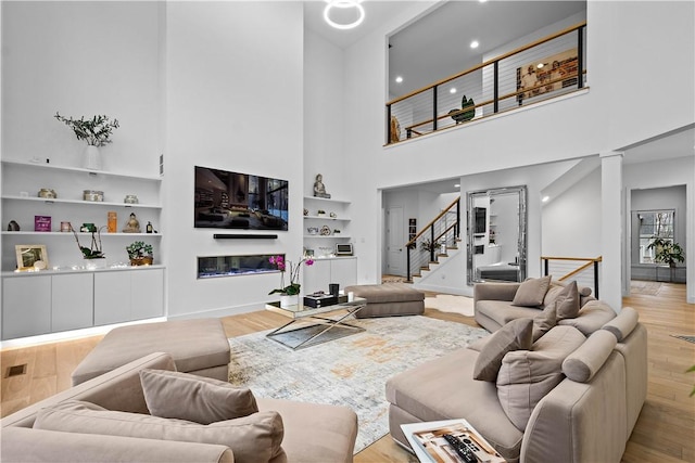 living room featuring built in shelves, stairs, baseboards, and wood finished floors