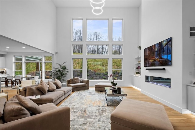 living room with a glass covered fireplace, recessed lighting, a high ceiling, light wood finished floors, and baseboards