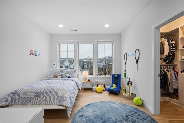 bedroom featuring recessed lighting, a walk in closet, visible vents, and wood finished floors