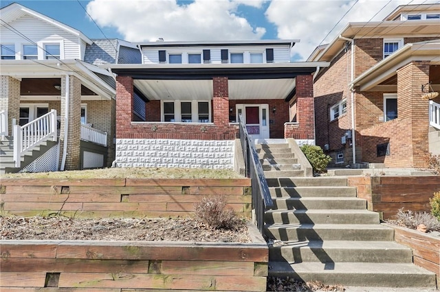 townhome / multi-family property featuring stairs, covered porch, and brick siding