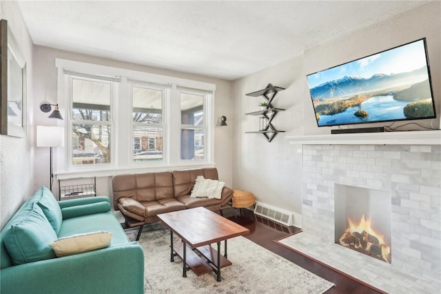 living area with visible vents, a brick fireplace, baseboards, and wood finished floors