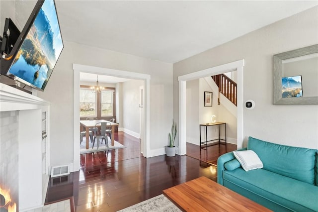 living room with visible vents, wood finished floors, stairway, an inviting chandelier, and baseboards