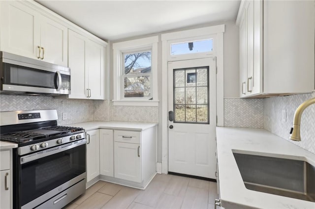 kitchen with backsplash, light countertops, appliances with stainless steel finishes, white cabinetry, and a sink