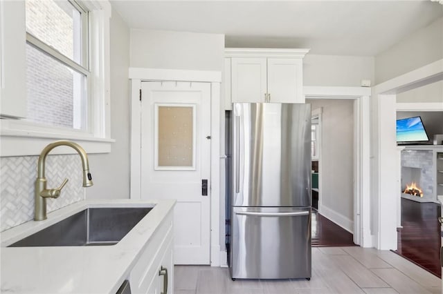 kitchen with a sink, white cabinetry, freestanding refrigerator, a lit fireplace, and decorative backsplash