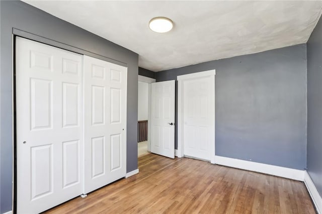 unfurnished bedroom with a closet, baseboards, and light wood finished floors