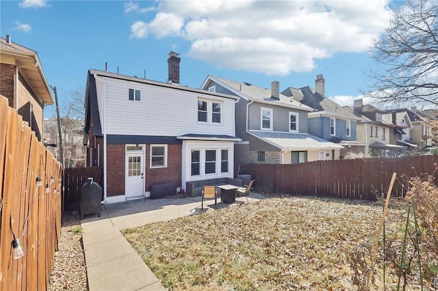 back of house with brick siding, a residential view, a chimney, a fenced backyard, and a patio