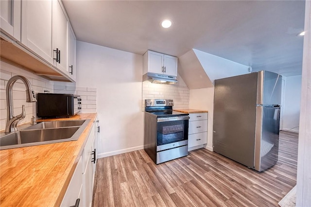 kitchen featuring under cabinet range hood, butcher block counters, light wood-style flooring, stainless steel appliances, and a sink