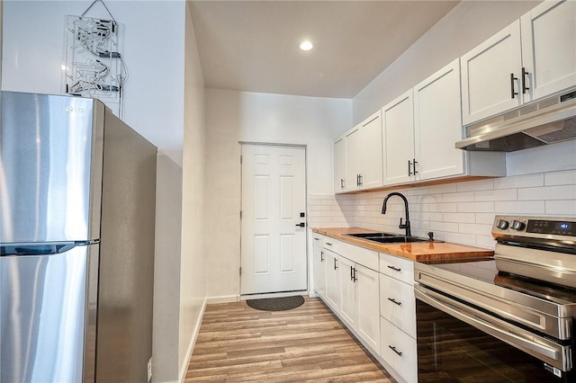 kitchen with light wood finished floors, a sink, stainless steel appliances, under cabinet range hood, and backsplash