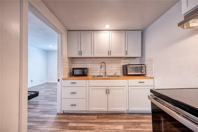 kitchen featuring light wood finished floors, backsplash, black microwave, white cabinetry, and a sink