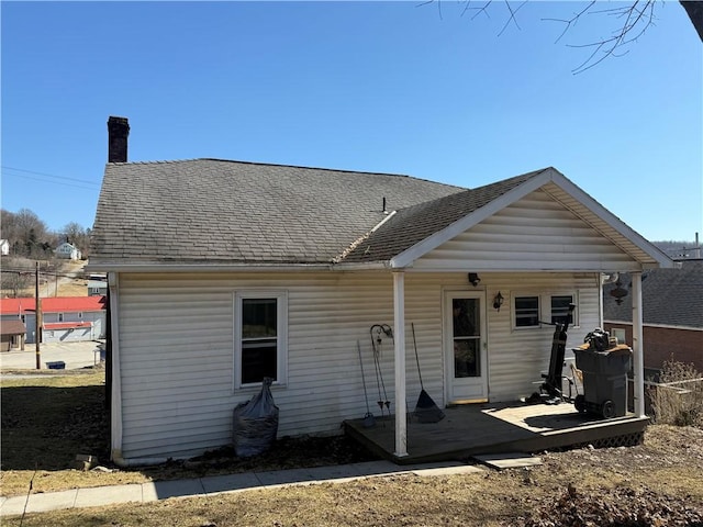 back of house featuring roof with shingles and a chimney