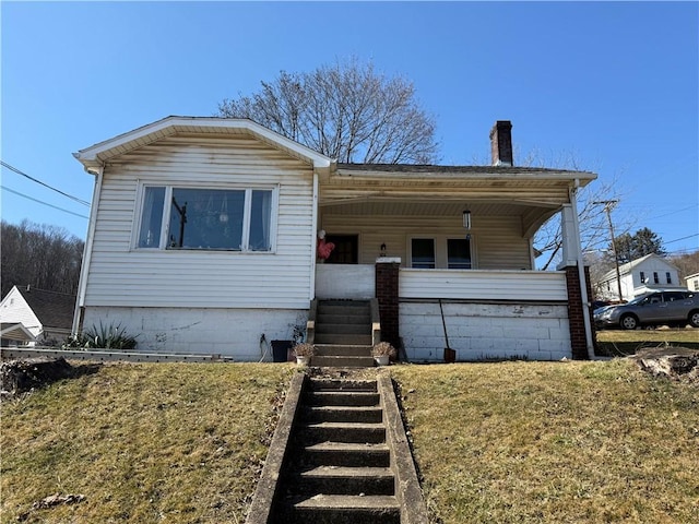 view of front of home featuring a porch, a front yard, and a chimney