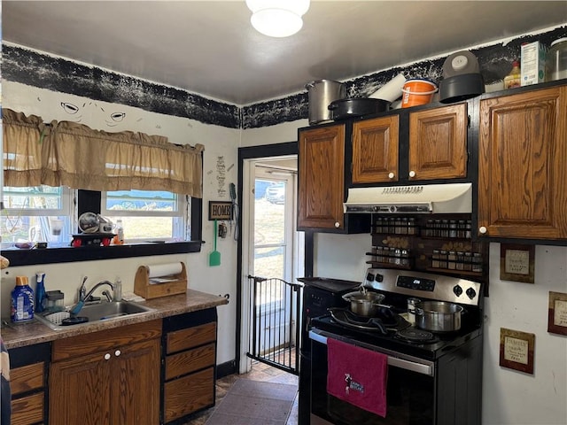 kitchen with under cabinet range hood, stainless steel electric range oven, brown cabinets, and a sink