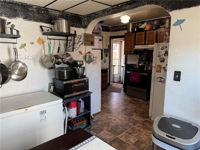 kitchen with arched walkways, stone finish floor, dark brown cabinets, under cabinet range hood, and appliances with stainless steel finishes