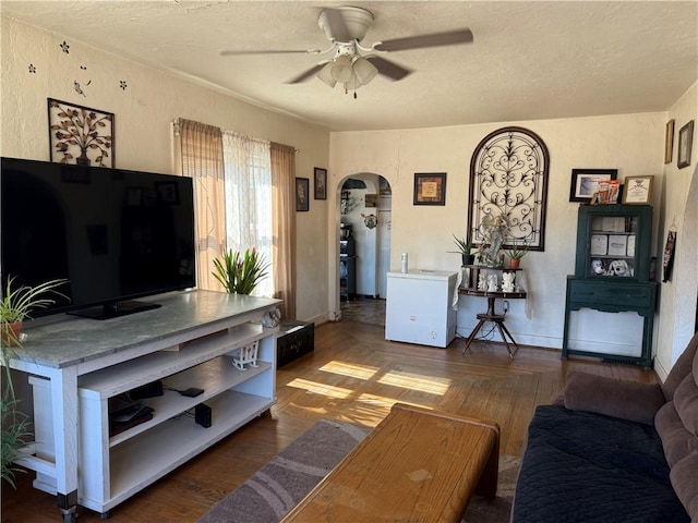 living area with baseboards, arched walkways, a textured ceiling, and a ceiling fan