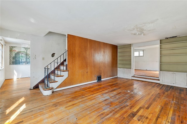 unfurnished room featuring built in shelves, hardwood / wood-style floors, and stairs