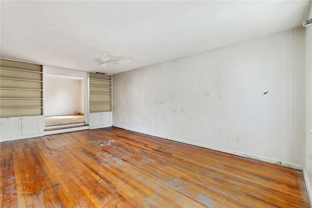 spare room featuring built in shelves and hardwood / wood-style floors