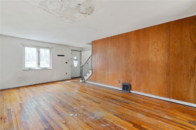 unfurnished living room with hardwood / wood-style floors, stairs, baseboards, and visible vents