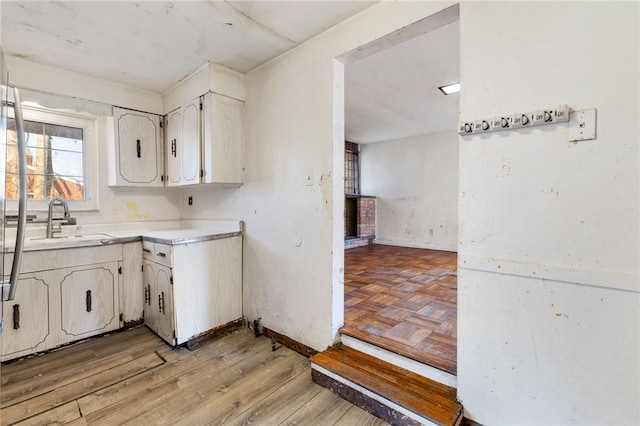 kitchen with baseboards, light wood-type flooring, light countertops, white cabinetry, and a sink