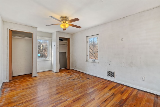 unfurnished bedroom with visible vents, multiple windows, and hardwood / wood-style floors