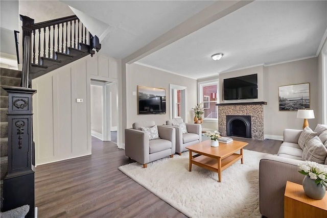 living area with baseboards, wood finished floors, a tiled fireplace, and crown molding