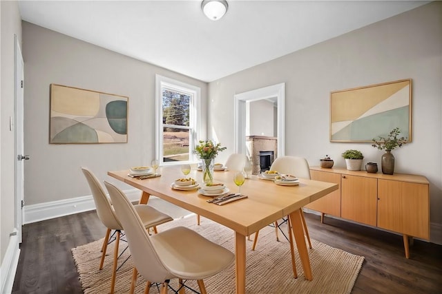 dining area with a fireplace, dark wood-style floors, and baseboards