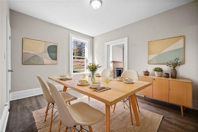 dining space featuring baseboards, a fireplace, and dark wood-style flooring