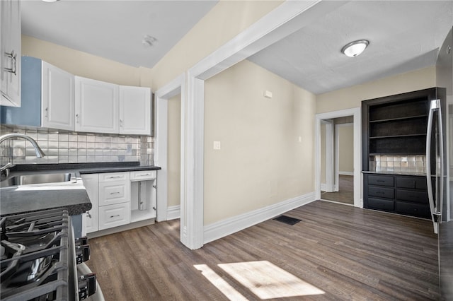 kitchen featuring a sink, tasteful backsplash, dark countertops, white cabinets, and dark wood-style flooring