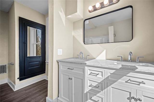 bathroom with a sink, baseboards, wood finished floors, and double vanity