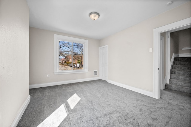carpeted spare room with stairway, visible vents, and baseboards