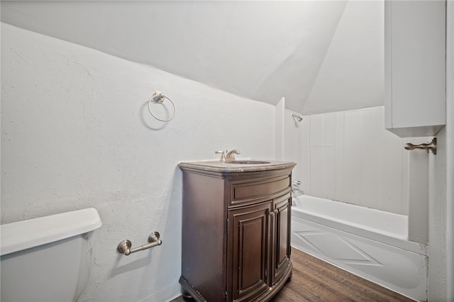 bathroom featuring vanity, washtub / shower combination, wood finished floors, vaulted ceiling, and toilet