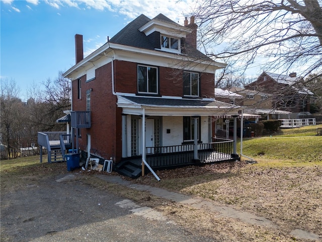 view of front of property featuring brick siding, covered porch, and a chimney