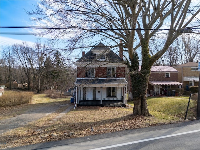 american foursquare style home with aphalt driveway, covered porch, a chimney, and a front yard
