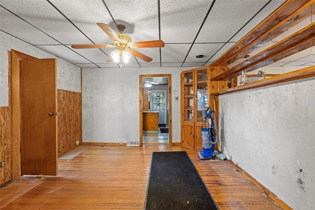 unfurnished room featuring hardwood / wood-style flooring, a ceiling fan, a wainscoted wall, and a paneled ceiling