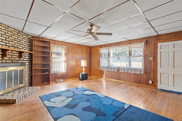 exercise area featuring ceiling fan, a drop ceiling, wood walls, a fireplace, and hardwood / wood-style flooring