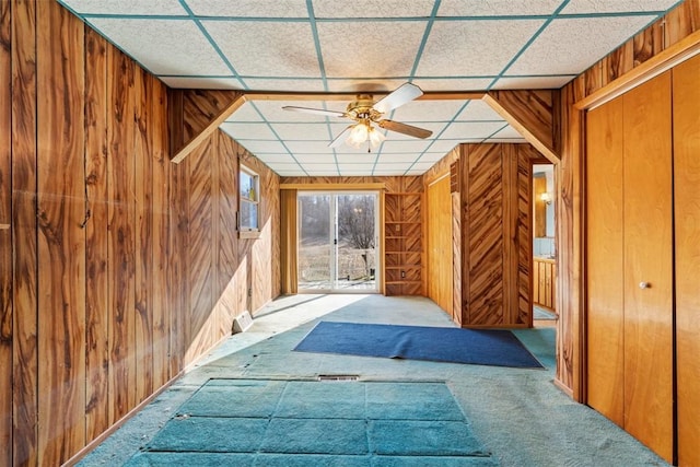 corridor with a drop ceiling, carpet flooring, and wood walls