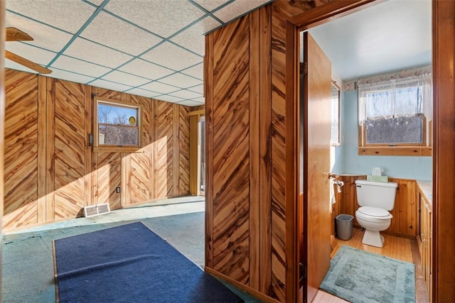 bathroom featuring visible vents, wood walls, toilet, and a paneled ceiling