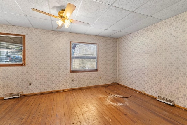 empty room featuring a ceiling fan, visible vents, wallpapered walls, a paneled ceiling, and wood-type flooring